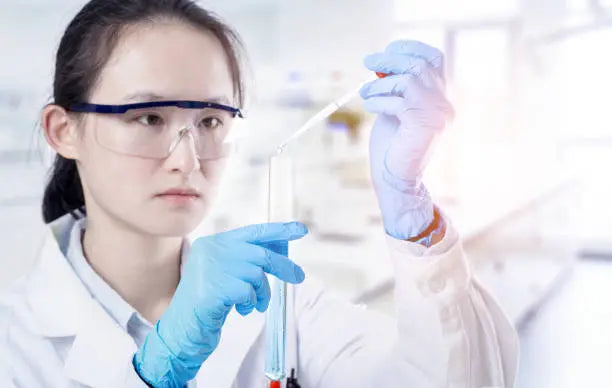 Person in a lab coat and gloves holding a test tube with a blurred background